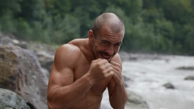 muscular man is training punches in nature and posing for camera, looking forward