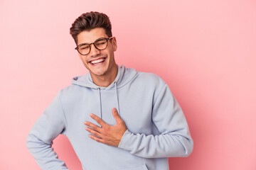 Young caucasian man isolated on pink background laughing keeping hands on heart, concept of happiness.