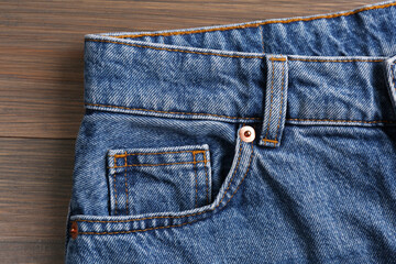 Stylish blue jeans on wooden background, closeup of inset pocket