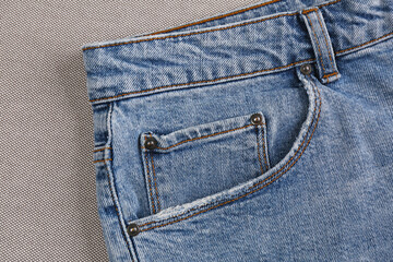 Stylish light blue jeans on grey fabric, closeup of inset pocket