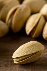 Close up of single pistachio in front of heap of salted, roasted green pistachio nuts snack over wooden background, healthy food snack
