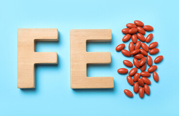 Wooden letters FE and pills on light blue background, flat lay. Anemia treatment