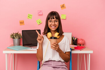 Young mixed race woman preparing a exam in the room holding a coffee isolated on pink background smiling and pointing aside, showing something at blank space.