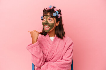 Young mixed race woman getting pretty in a house isolated on pink background points with thumb finger away, laughing and carefree.