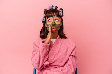 Young mixed race woman getting pretty in a house isolated on pink background is saying a secret hot braking news and looking aside