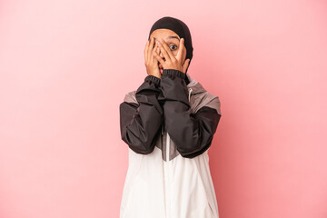 Young Arab woman with sport burqa isolated on pink background blink through fingers frightened and nervous.