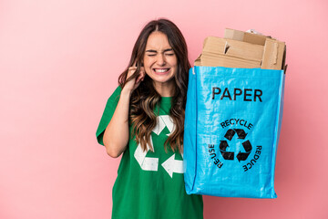 Young caucasian woman recycled paper isolated on pink background covering ears with hands.