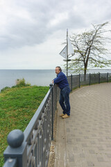 a middle-aged Man stands on the waterfront of the resort city on a cloudy spring day. Calm sea in the off-season