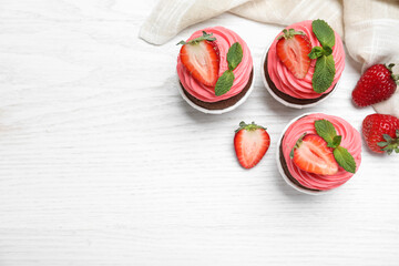 Sweet cupcakes with fresh strawberries on white wooden table, flat lay. Space for text