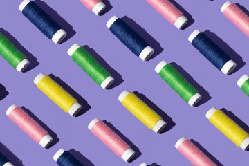 sewing thread in pink yellow, green and blue color . minimal  pattern concept on purple background.