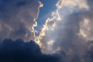 sunlight breaking through white and dark clouds in the blue sky