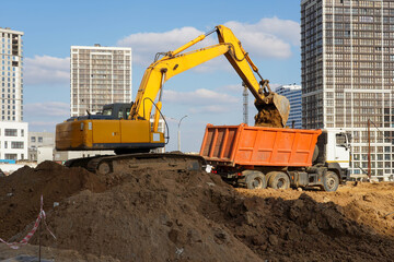 Photo of an excavator and a truck at the construction site of multi-storey buildings in the city