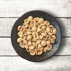 Traditional barley orecchiette pasta from Puglia on a rustic bowl over a white aged table.