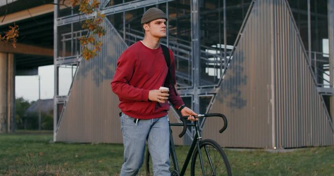 A young man walks through the autumn city, driving a bicycle in his hands