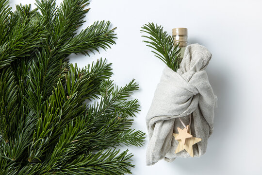 Zero Waste Merry Christmas Winter Gift Wrapping, Bottle In Japanese Furoshiki Style In Linen Fabric, Decorated With Natural Green Branches Of Fir Nobilis. Concept Eco-friendly Creative Package