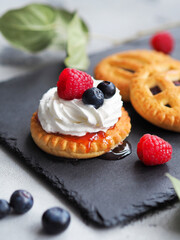 Sweet cookie with whipped cream and fresh berries on stone tray.