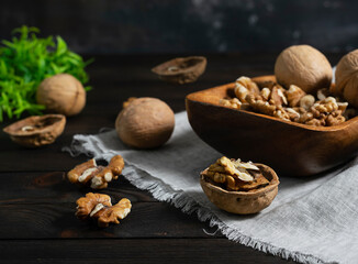 Peeled walnuts in a wooden bowl on a dark wooden background. Whole nuts and green leaves in the background