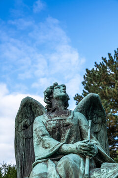 Imposante Engelsfigur mit Trompete  sitzt auf einem Grabstein und schaut zum Himmel