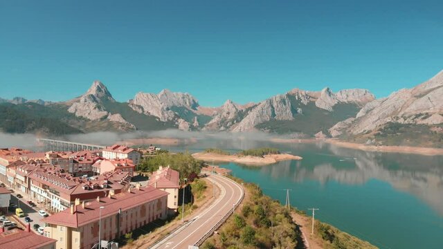aerial drone shot of a swamp located in the town of Ria&ntilde;o, a village with a road with a bridge that divides the lake on a sunny day with the stone mountains in the background