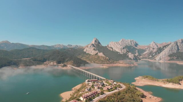 aerial drone shot of a swamp located in the town of Ria&ntilde;o, a village with a road with a bridge that divides the lake on a sunny day with the stone mountains in the background