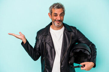 Middle age biker caucasian man holding helmet isolated on blue background  showing a copy space on...