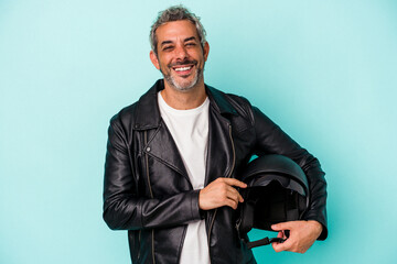Middle age biker caucasian man holding helmet isolated on blue background  laughing and having fun.