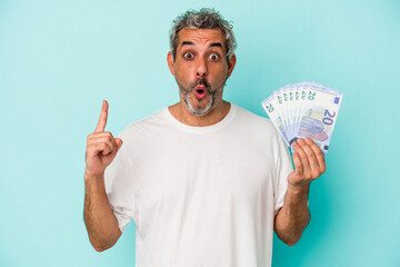 Middle age caucasian man holding bills isolated on blue background  having some great idea, concept of creativity.