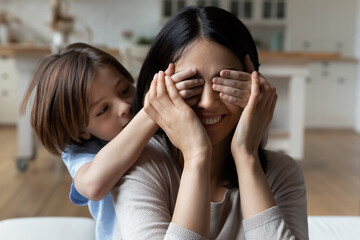 Playful kid covering mom eyes with hands, preparing surprise present. Joyful happy mum and little...