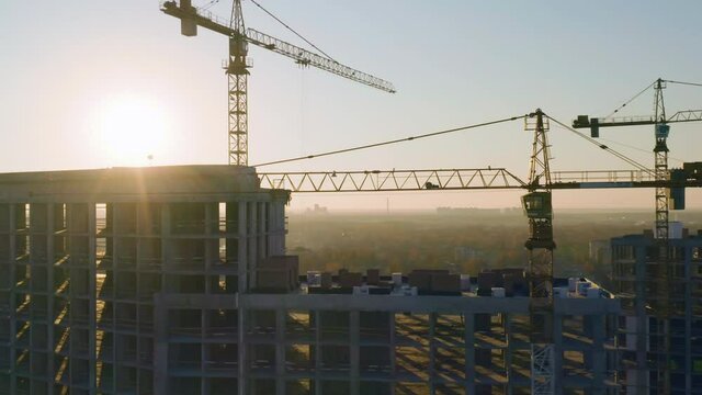 Aerial panoramic view of the high-rise apartment buildings (block of flats) under construction with tower cranes at sunset