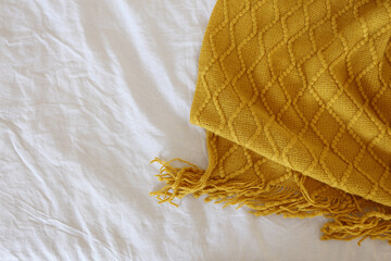 Fototapeta na wymiar cozy mustard-colored knitted blanket on a white linen sheet