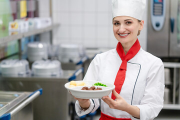 Proud cook showing plate with food in commercial kitchen of canteen