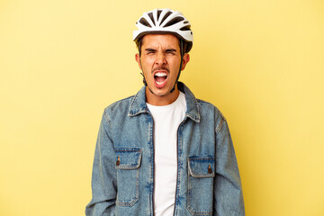 Young mixed race man wearing a helmet bike isolated on yellow background screaming very angry and aggressive.