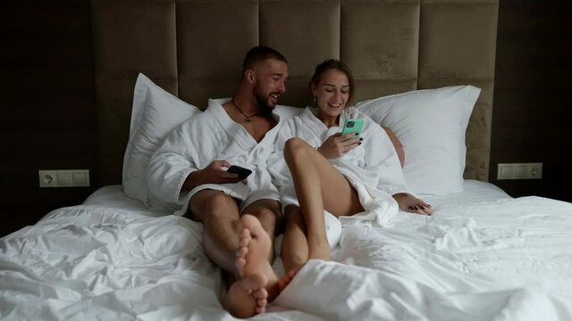 couple in bed in weekend morning, using modern smartphones and communicating