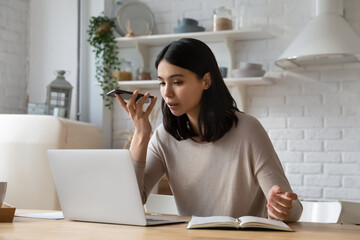 Serious young Asian student woman recording, sending audio message on smartphone, using voice...