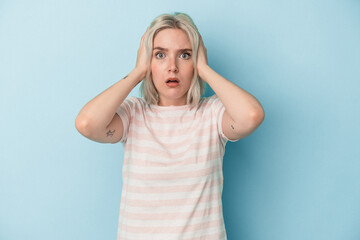 Young caucasian woman isolated on blue background covering ears with hands trying not to hear too loud sound.