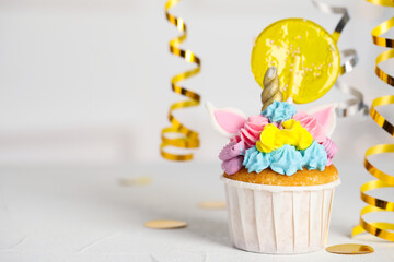 Cute sweet unicorn cupcake with yellow lollipop on white table, space for text. Festive treat