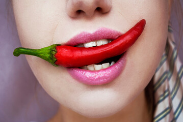 Woman's bright pink lips and chili peppers. Beautiful woman is biting a red pepper, close-up.