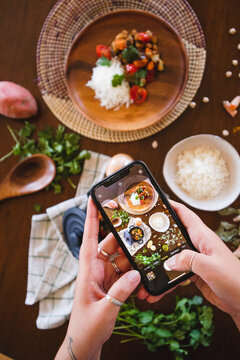 woman taking picture of food on the table vegan food rice and vegetables carrots sweet potato tomatoes coriander turmeric onions and chickpeas food photography