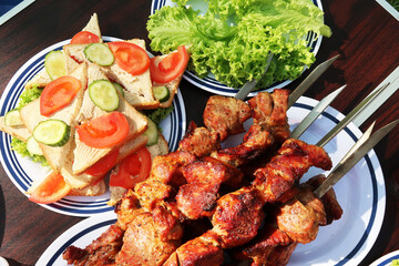 Top view of barbecue skewers on a plate with sandwiches on a table in a summer park