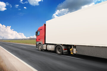Truck with a white trailer with blank space for text on a road in motion against a sky with clouds