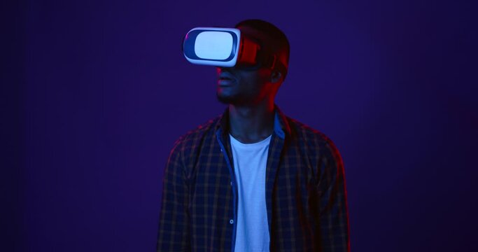 Futuristic technologies. African american man wearing virtual reality glasses watching video, neon lights background