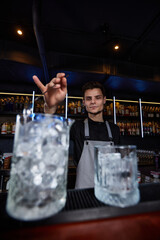 Fototapeta na wymiar Barman stirring ice cubes in cocktail glass with spoon