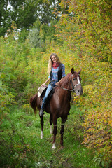 Fototapeta premium Beautiful cowgirl ride her horse in autumn country road at sunset