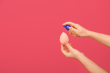 Fototapeta premium Woman putting foundation on makeup sponge on color background