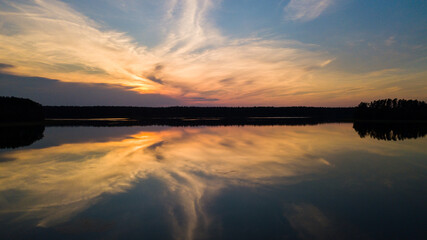 Beautiful sundown over the lake. Mirror image of the sunset in a summer day. Blue sky, orange clouds.