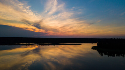 Beautiful sundown over the lake. Mirror image of the sunset in a summer day. Blue sky, orange clouds. Orange sky.
