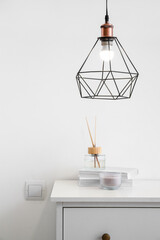 Reed diffuser with books on shelf and glowing lamp near white wall