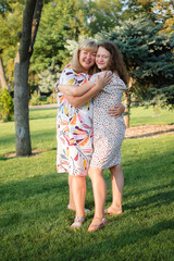 Female portrait of a beautiful plus size blond, blue-eyed mother and daughter in the park during summer. Family day, happy people concept