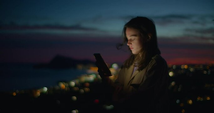 Cinematic dusk shot in dark setting of young woman look at phone and scroll through different pages and apps. Student or freelancer use technology for online shopping or job search