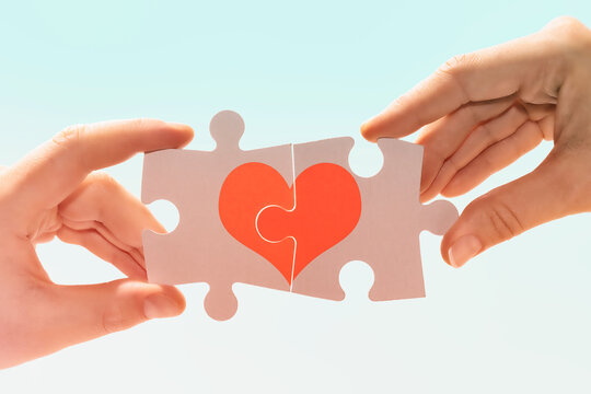 A man and a woman connect pieces of a puzzle with a picture of a heart. Compatibility between man and woman.